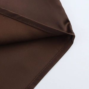 Détail de l'ourlet à double surpiqûre sur chemise satinée marron foncé au tissu lisse