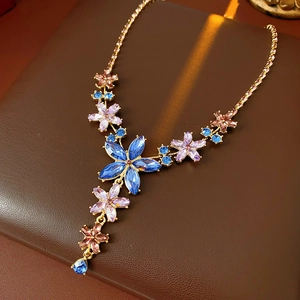 Détail du collier floral vintage doré avec cristaux bleus et violets sur support en cuir brun