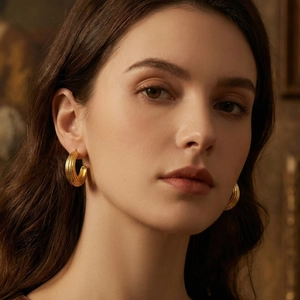 Boucles d'oreilles créoles C dorées à rayures sur mannequin sous lumière vintage