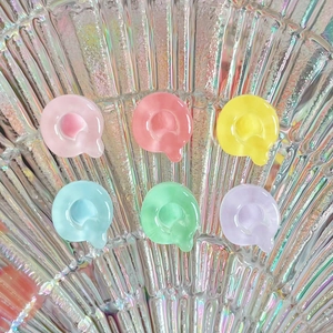 Close-up of translucent Q-shaped resin charms in pastel colors on an iridescent plate