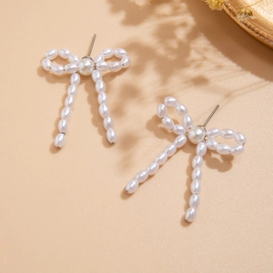 Macro detail of elegant bow earrings featuring white pearls and silver metal studs