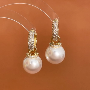 Detailed view of a gold pearl earring featuring zircon pave accents and a glossy surface