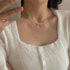 Close-up of a 925 silver bow necklace with pearls on a model wearing a white cardigan