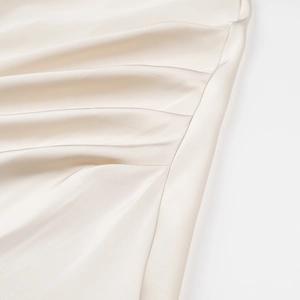 Detail shot of champagne satin dress showing ruched side texture and silky fabric finish