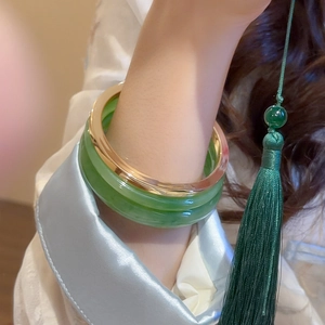 Close-up of stacked jade green resin bangle and gold metallic bracelet on wrist
