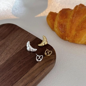 Detail of minimalist 925 silver croissant and pretzel stud earrings on wooden board