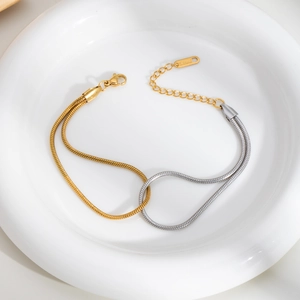 Detail of two-tone gold and silver snake chain bracelet with lobster clasp in a ceramic tray
