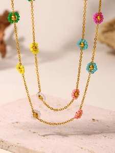 Close-up of colorful floral beaded necklace with golden chain on textured stone