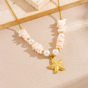 Gold starfish pendant necklace with white pearls and pink stones on a textured surface