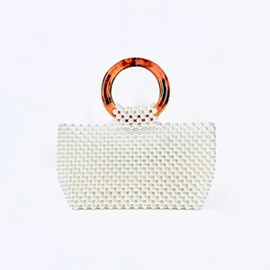 Detail of handmade pearl beaded handbag with amber resin ring handles on white background