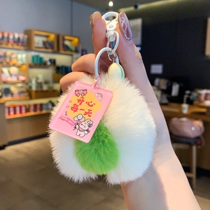 Close-up of a plush avocado keychain featuring green balls and a pink Happy Day tag