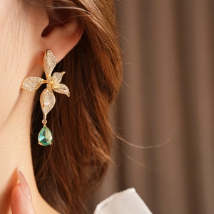 Close-up of golden vintage flower earrings with green teardrop stones on model