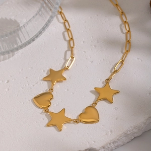 Collier trombone doré avec pendentifs cœur et étoile sur une surface en marbre blanc