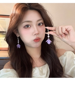 Detailed view of floral pearl earrings with purple petals and silver needles on model