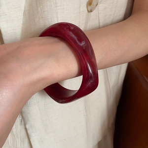 Close-up of deep red marble pattern resin bangle worn on a textured fabric background