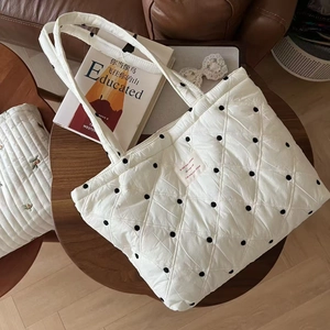 Detail of quilted down tote bag with black polka dots and French text patch on white fabric
