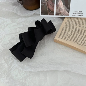 Detail of elegant black satin multi-layer bow hair clip on a minimalist white backdrop