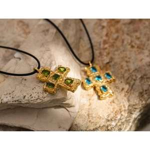 Macro view of gold 18k cross pendants with green and blue gems on black wax cords