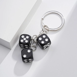 Detail of creative black dice charms attached to a metallic keychain on a white surface