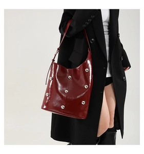 Red patent leather shoulder bag with metallic studs worn by a model in a black outfit