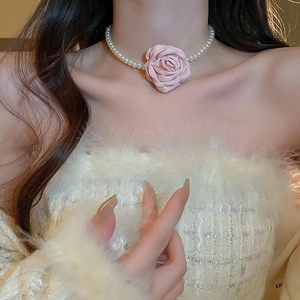 Close-up of pink fabric rose pendant and white faux pearl beads on a model's neck