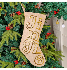 Close-up of burlap Christmas stocking with Jingle gold sequins hanging on a tree