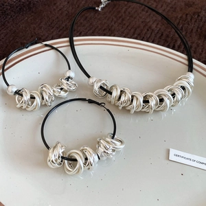 Detail of silver knot beads and black cord jewelry set displayed on a ceramic dish