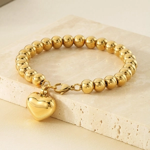 Détail macro du bracelet à billes dorées avec pendentif cœur sur marbre beige