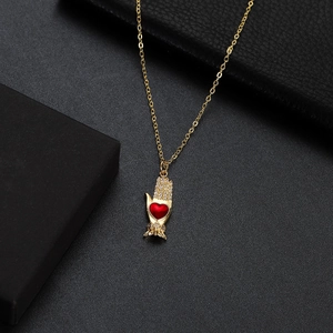 Macro detail of gold necklace with hand charm holding a red heart and zircon stones