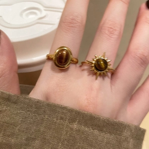 Detailed view of gold rings with tiger eye stone and starburst design on a finger
