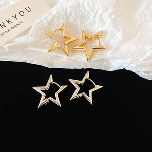 Macro shot of gold and silver hollow star-shaped hoop earrings on a textured background