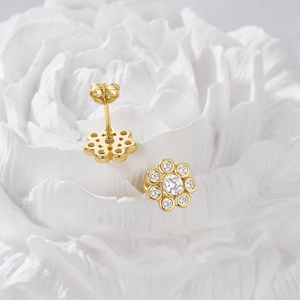Macro shot of gold floral stud earrings with white zircons on a ceramic flower base