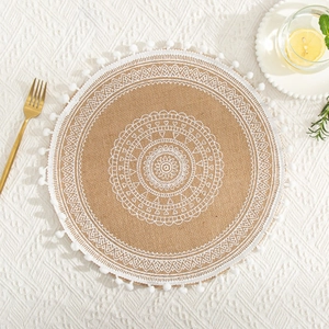 Detail of round jute placemat featuring white mandala lace embroidery and pompom tassel trim