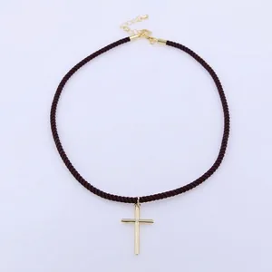 Dettaglio di una collana in corda marrone scuro con ciondolo a croce dorata e chiusura