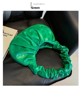 Close-up of vibrant green ruched PU leather handbag on a black leather chair with book