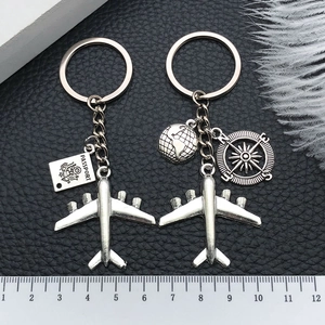 Silver metal keychain detail featuring airplane, passport, and globe charms with scale