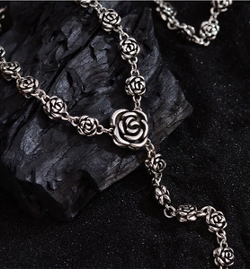Detail shot of vintage silver rose necklace on black charcoal and sand background