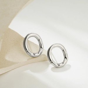 Close-up of silver irregular oval earrings with unique pleated texture on minimal backdrop