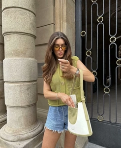Street style shot of green chunky knit sleeveless vest paired with blue denim shorts