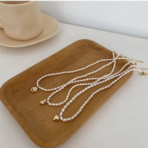 Detail of freshwater pearl necklaces with golden smile, bean and heart charms on wood tray