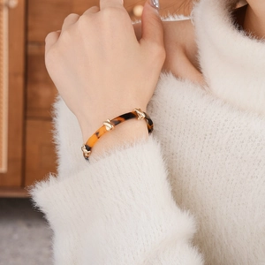 Detailed close-up of leopard resin bangle with gold knot accent on a beige knit sleeve