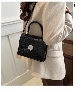 Detail of black faux crocodile leather crossbody bag with silver round metal buckle