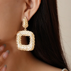 Golden geometric square earrings with wheat ear texture worn by a model in a close-up shot