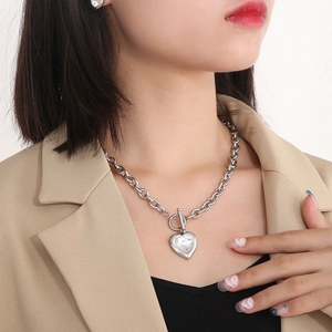 Gros plan d'un collier argenté avec fermoir OT et pendentif cœur en cristal sur mannequin