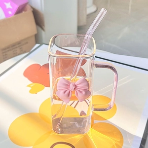 Detail of square glass mug with pink bow decoration and matching clear straw on a mat