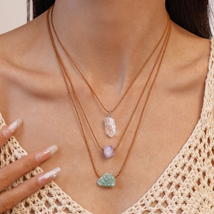 Close-up of bohemian layered necklace with clear, purple, and green raw crystal stones