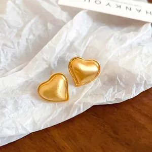 Matte brushed gold heart stud earrings displayed on white pleated paper and wooden base