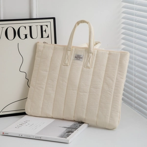 Close-up of cream quilted laptop sleeve with vertical stitching and top handle
