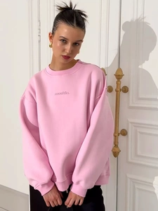 Detail of pink crewneck sweatshirt featuring black letter print and ribbed cuffs