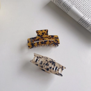 Detail view of acetate claw clips in amber tortoiseshell and creamy white marble patterns